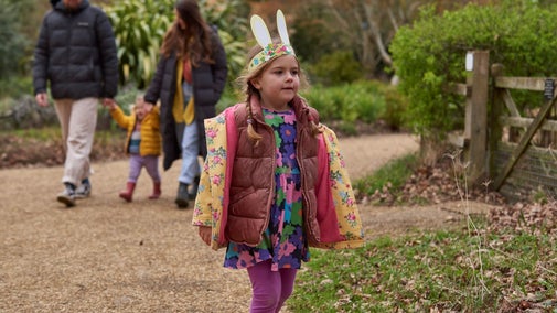 A girl wearing Easter bunny ears and her family walking along a path at Sheringham Park